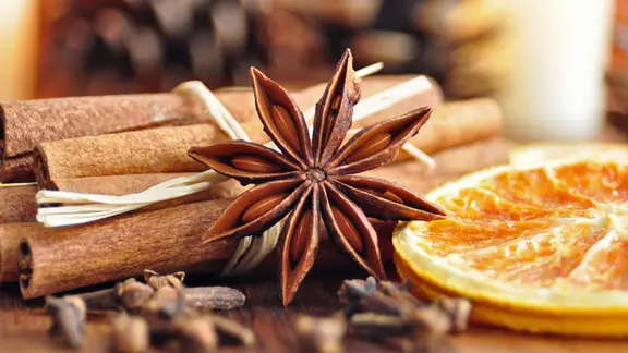 Sternanis, Nelken, Zimtstangen und eine getrocknete Orangen-Scheibe liegen auf einem Tisch.