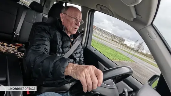 Ein älterer Herr sitzt am Steuer eines PKW.