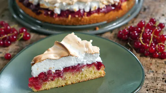 Johannisbeerkuchen mit Baiser steht angeschnitten auf einem blau/grünem Teller