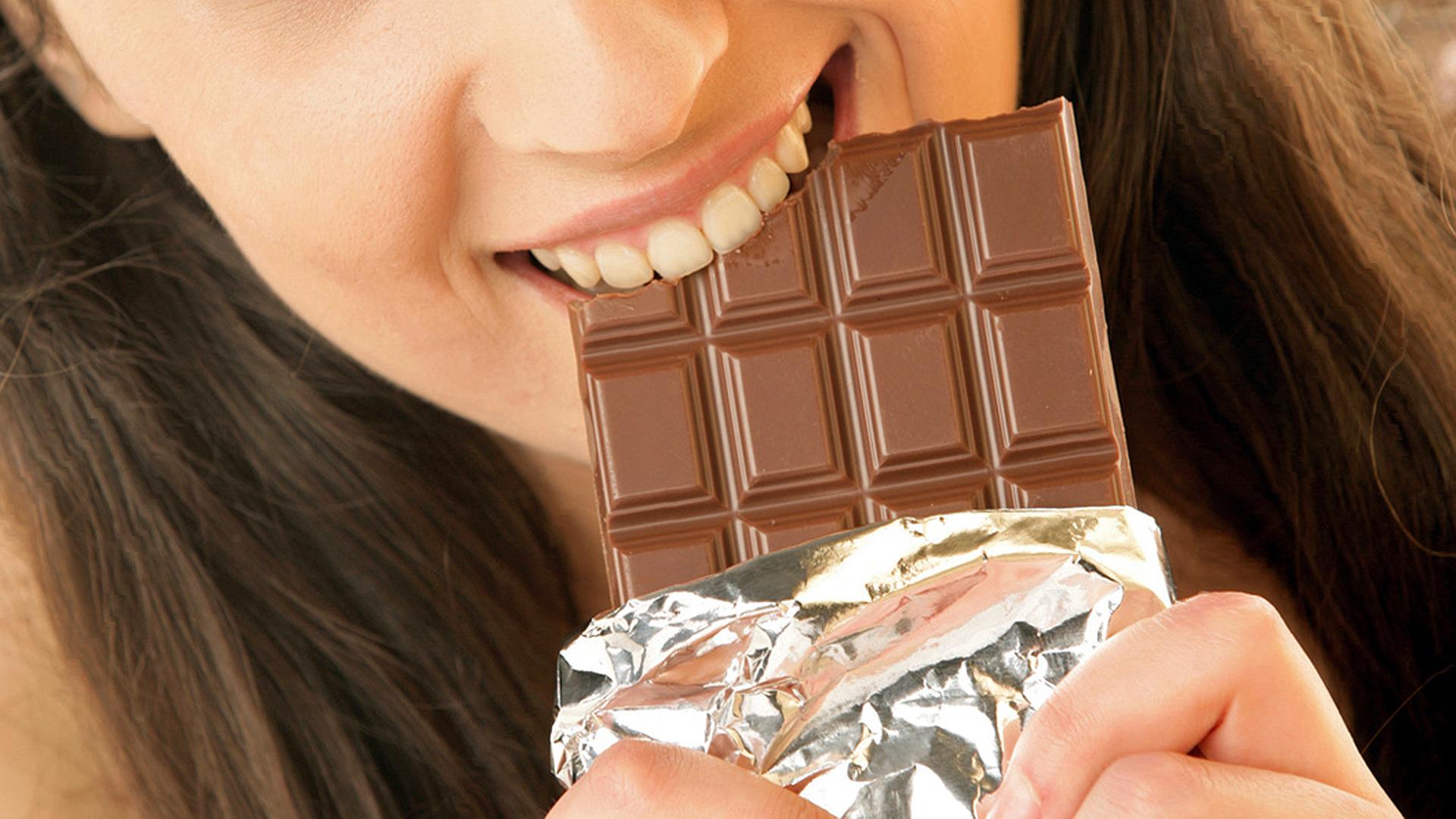 Eine junge Frau beißt in eine Tafel Schokolade. | Fotolia, studiovespa
