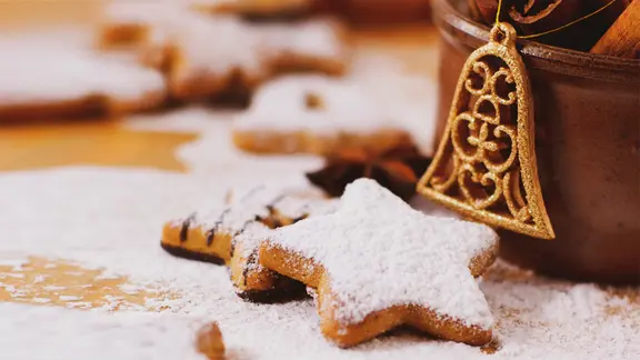 Mit Puderzucker bestäubte Kekse in Sternform liegen auf einem Holzbrett.