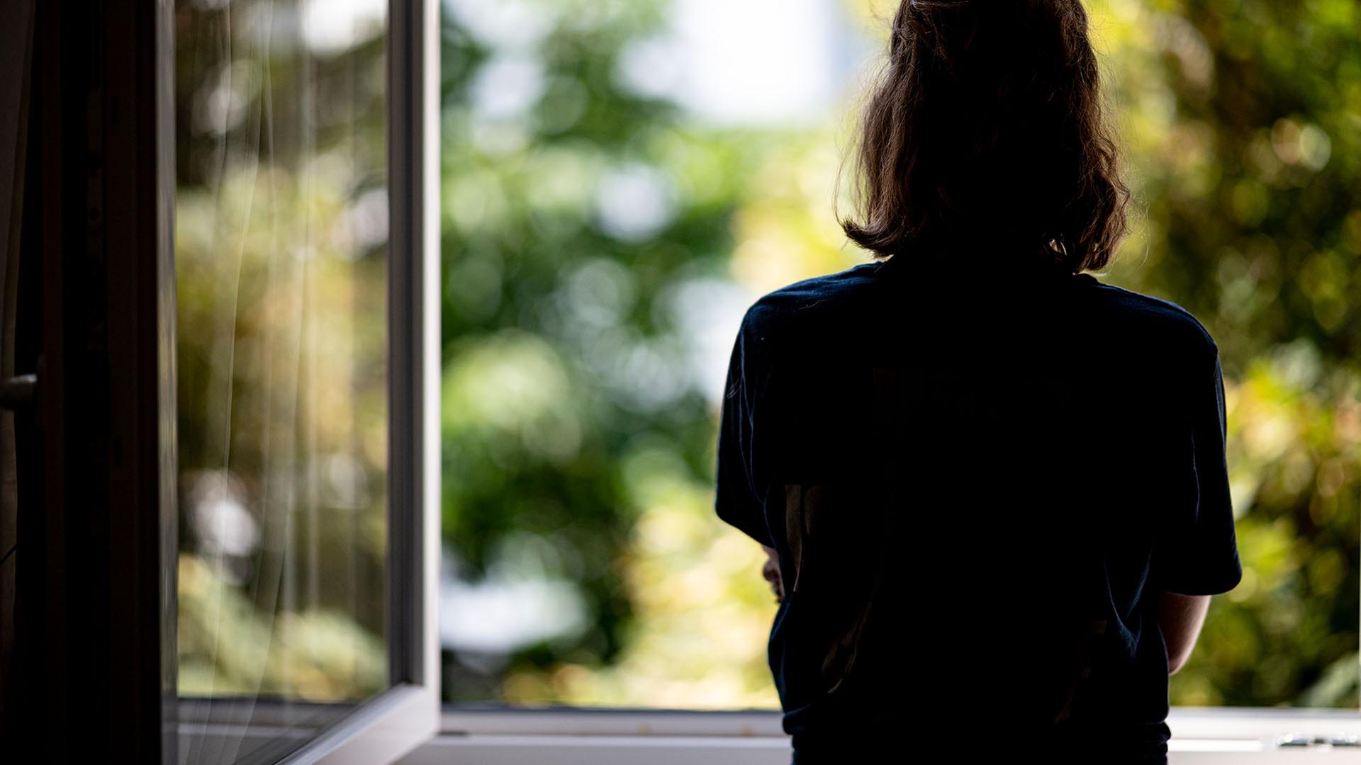 Eine Frau steht in ihrer Wohnung an einem Fenster. | picture alliance/dpa/Fabian Sommer, Fabian Sommer