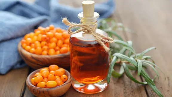 Zwei Holzschalen mit Sanddornbeeren und eine Flasche mit Sanddornöl