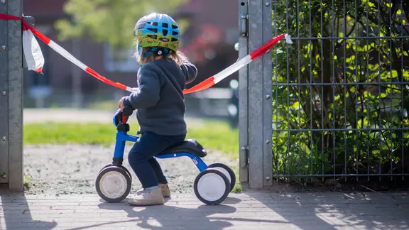 Ein Kind vor einem abgesperrten Spielplatz.