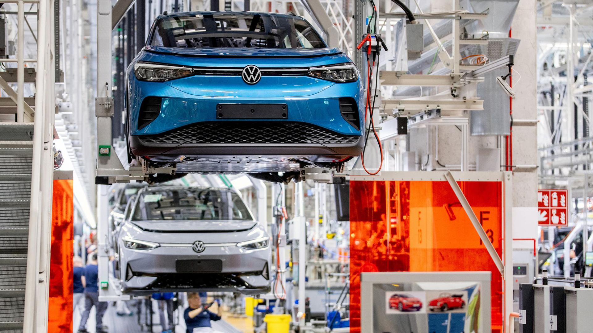 Mitarbeitende arbeiten im Werk von Volkswagen an einem Fließband an Fahrzeugen. | Hauke-Christian Dittrich/dpa