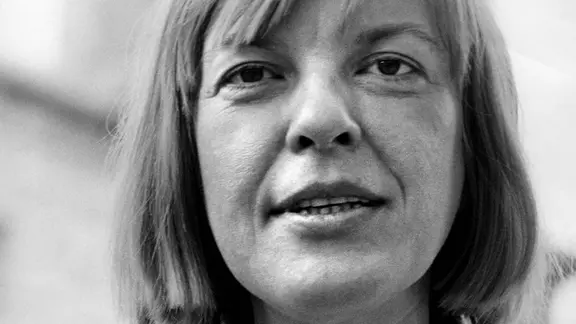 Μια γυναίκα γύρω στα σαράντα με μεσαίου μήκους ξανθά μαλλιά φαίνεται φιλική μπροστά από την κάμερα με καστανά μάτια. Το στόμα της είναι ελαφρώς ανοιχτό, σαν να θέλει να πει κάτι.