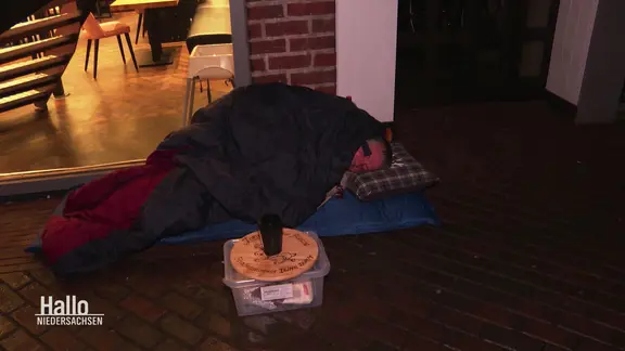 Der Obdachlose Jonny liegend in der Fußgängerzone in einem Schlafack und auf einer Luftmatratze.
