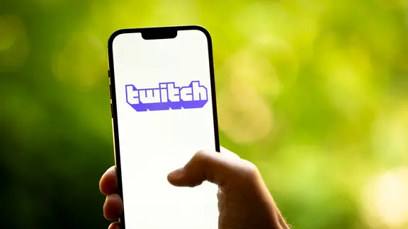 Eine Hand hält ein Smartphone in den Händen, auf dem Display ist das Twitch-Logo zu sehen.