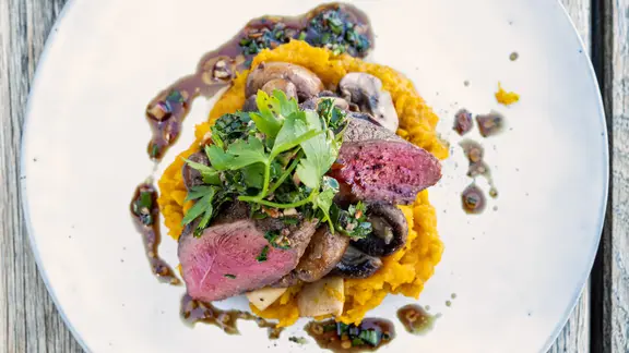 Kürbisstampf mit Rehkeulen-Steaks und Pilzen auf einem Teller angerichtet.