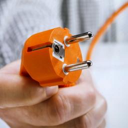 Hand hält den Stecker eines Elektrogerätes.