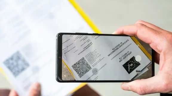 Ein Mann scannt mit seinem Smartphone den QR-Code seines Impfnachweises.