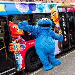 Eine als Krümelmonster verkleidete Person steht vor einem Linienbus der Hamburger Hochbahn, der anlässlich des 50-jährigen Jubiläum der Sesamstraße mit den Figuren Ernie (l.) und Bert beklebt ist.