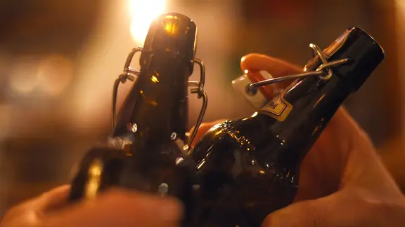 Zwei Menschen stoßen in einer Kneipe mit Flaschen-Bier an.