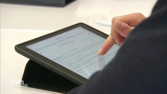 Eine Person bedient ein Tablet mit einem Stylus-Stift und liest einen Text auf dem Bildschirm.