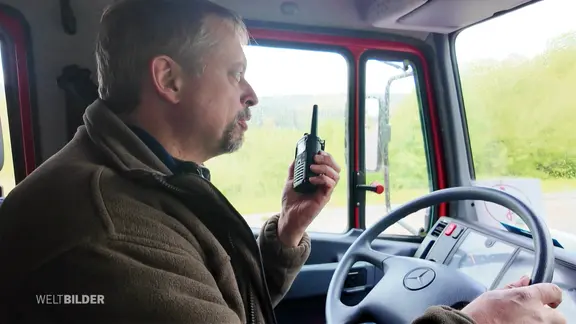 Ein Mann mit einem Handfunkgerät am Steuer eines Fahrzeugs.