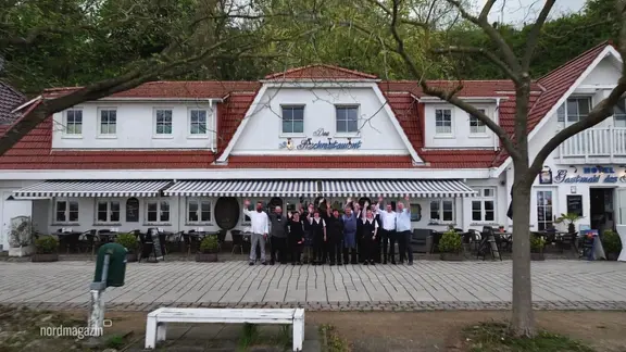 Das Team des Restaurants "Gastmahl des Meeres" steht winkend vor dem Gasthaus.