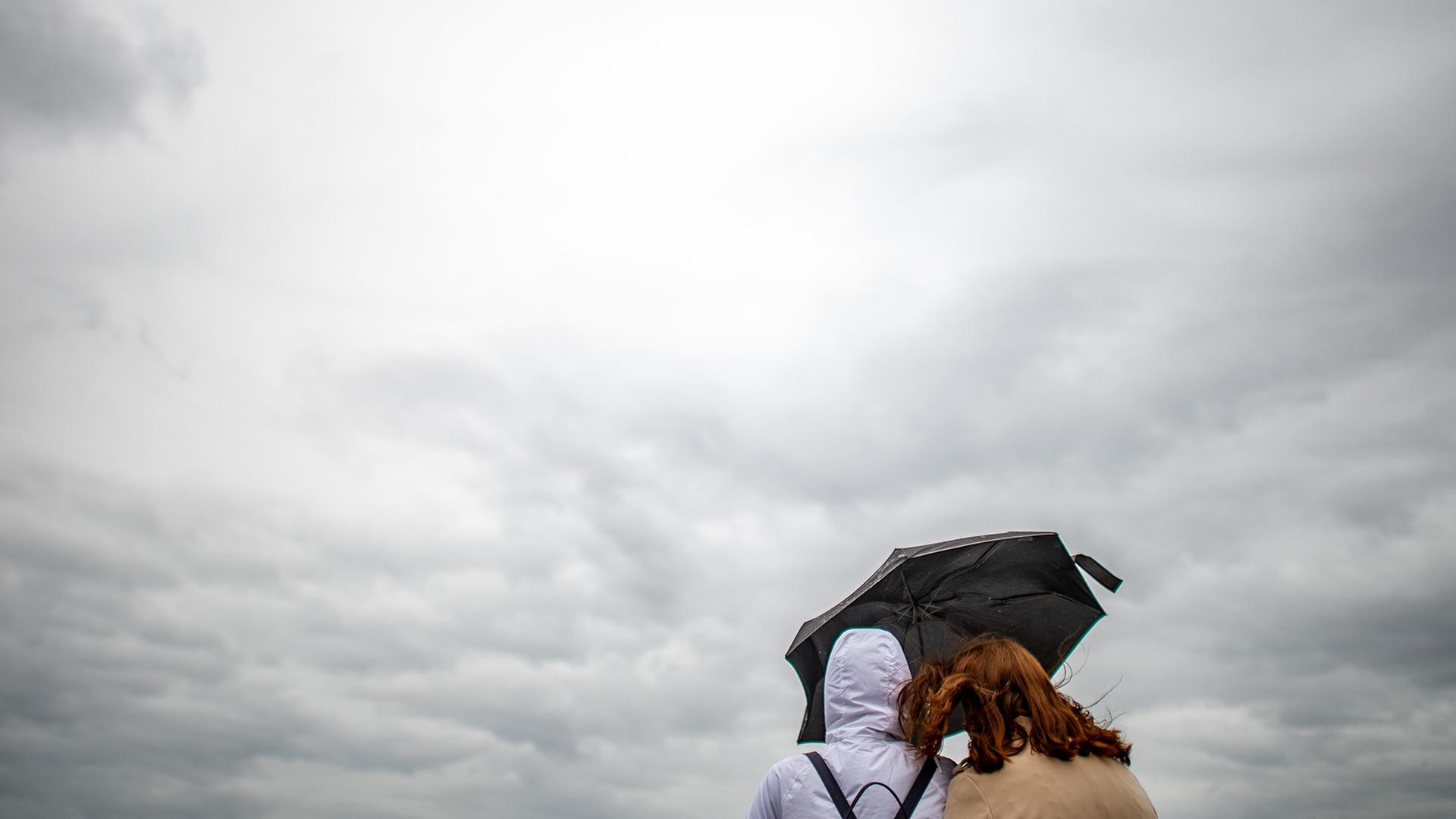 Zwei Frauen stehen unter einem Regenschirm und blicken auf dunkle Wolken. | picture alliance/Jonas Güttler