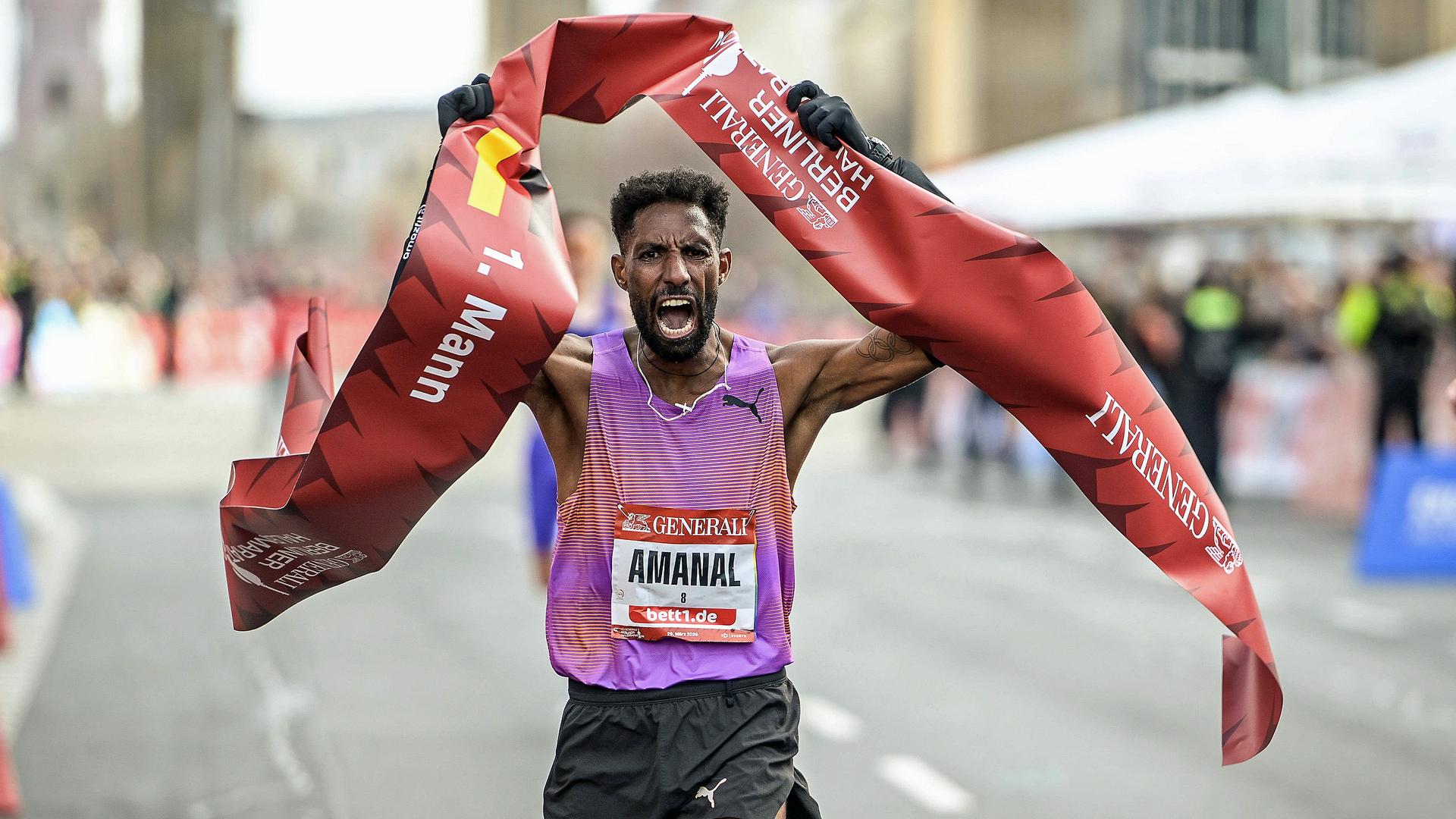 Amanal Petros hält ein rotes Band in die Luft. | IMAGO / Jan Huebner