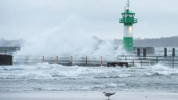 Wellen schlagen während eines Sturms am Strand an der Ostsee an einem Leuchtturm an der Einfahrt zur Trave hoch.
