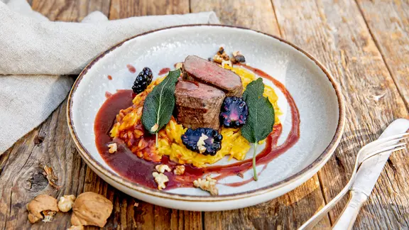 Rehrücken mit Kürbis-Risoni und Brombeeren auf einem Teller angerichtet.