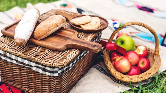 Ein Picknickkoffer mit Brot und ein Korb mit Äpfeln auf einer Decke im Gras