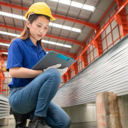 Eine Frau kniet neben Stahlplatten in einer Werkhalle