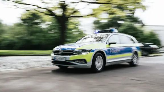 Ein Polizeiauto in Unschärfe fährt mit Blaulicht eine Straße entlang.