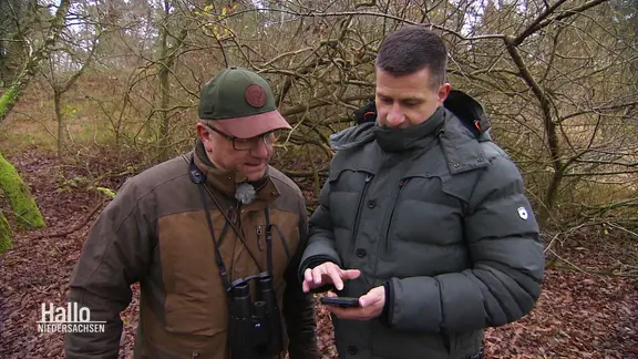 Zwei Jäger schauen zusammen auf ein Samrtphone im Wald.