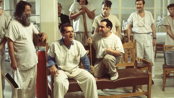 Jack Nicholson und Danny DeVito sitzen, von anderen Darstellern umringt, auf einer Bank. 