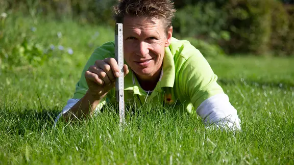 Peter Rasch liegt im Gras und hält einen Zollstock in der Hand.
