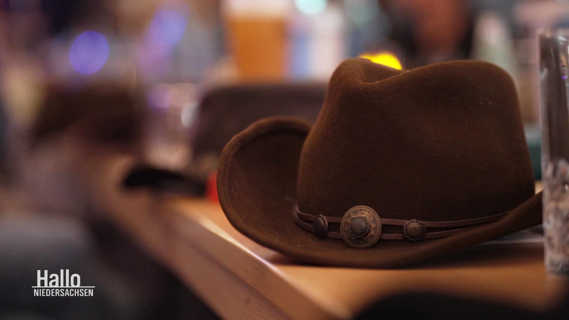 Ein Cowboyhut vor tanzenden Personen. | Screenshot