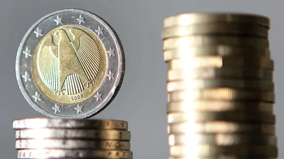 Ein Stapel mit Ein-Euro-Münzen steht neben einem Stapel mit Zwei-Euro-Münzen.