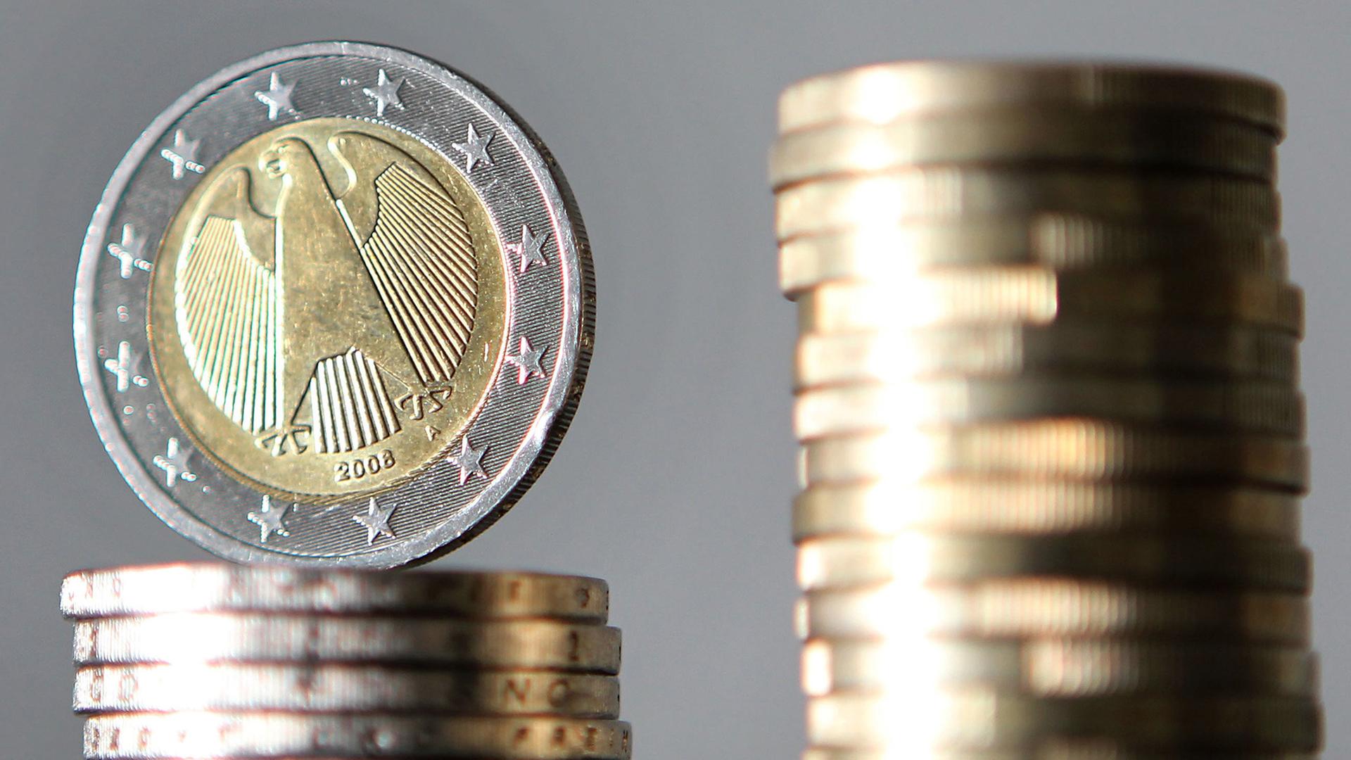Ein Stapel mit Ein-Euro-Münzen steht neben einem Stapel mit Zwei-Euro-Münzen. | picture alliance/dpa, Oliver Berg
