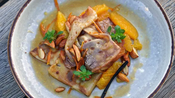 Crêpes Suzette mit Orangen und Mandeln auf einem Teller serviert.