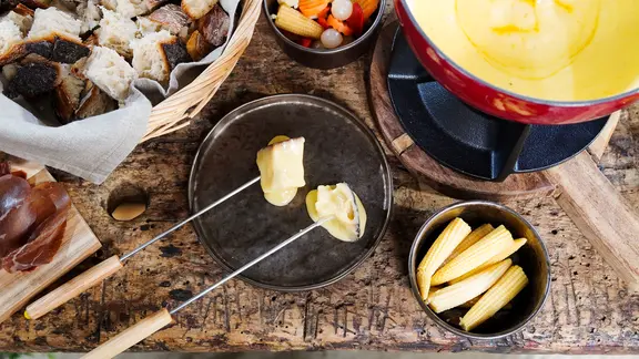 Ein Rechaud mit Käsefondue, ein Korb mit Brotwürfeln und zwei Schalen mit Pickles