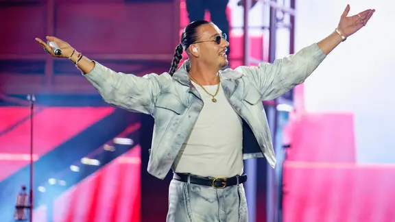 Der Rapper Apache 207 steht mit ausgebreiteten Armen während einer Show auf der Bühne und schaut zur Seite