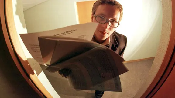 Ein Mann steht vor einer Haustür mit Papieren in der Hand.