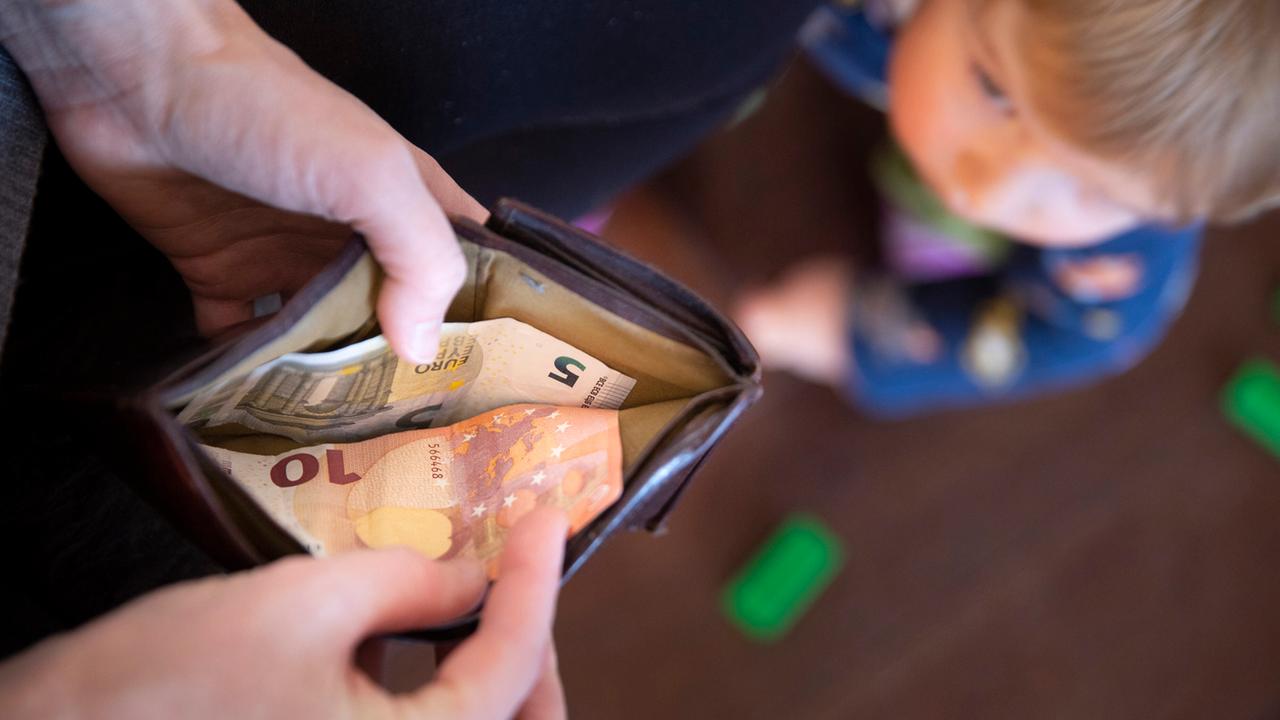 Eine Frau zählt Geld im Portemonnaie, ein Kind schaut zu.
