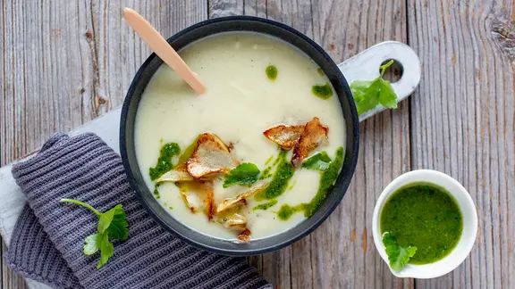 Eine Schüssel mit Wurzelcremesuppe, Pesto und Topinamburchips.