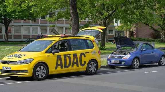 Ein ADAC Auto steht am Straßenrand mit geöffnetem Kofferraum, dahinter ein blaues Auto mit geöffneter Motorhaube.