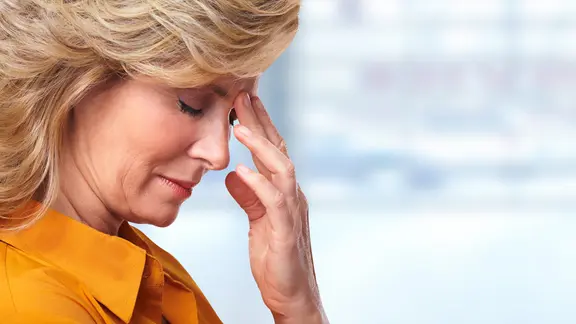 Eine Frau fasst sich an die Stirn.