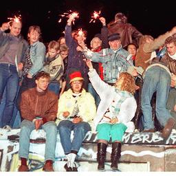 Menschen sitzen am 10. November 1989 auf der Berliner Mauer und feiern