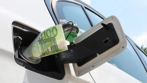 Ein Geldschein in einer Auto-Tankklappe.