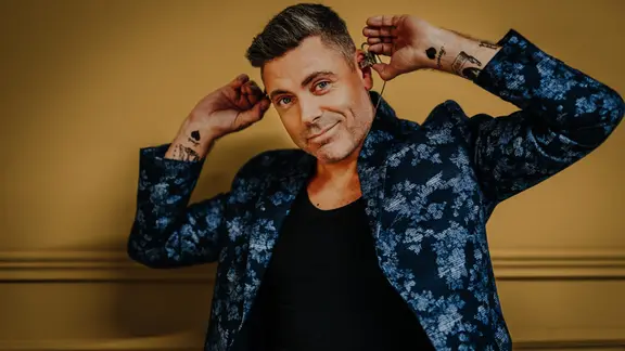 Ein Mann mit angewinkelten Armen blickt lächelnd in die Kamera