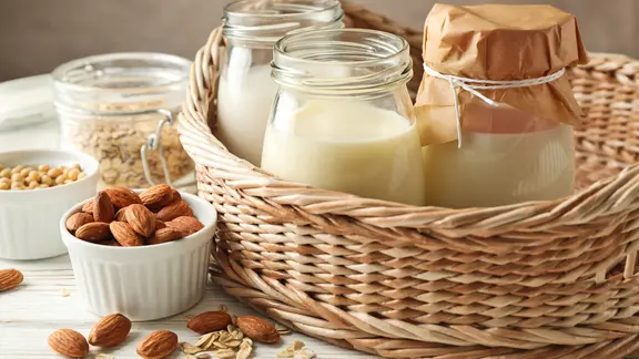 Gläser mit veganen Joghurtersatzprodukten, daneben Mandeln und Hafer.