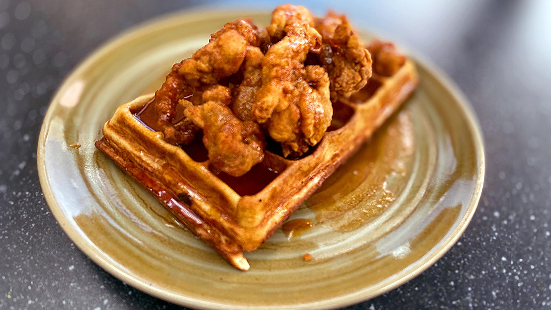 Frittiertes Hähnchen mit Waffeln und scharfer Honig-Buttersoße auf einem rustikalen Teller angerichtet | NDR