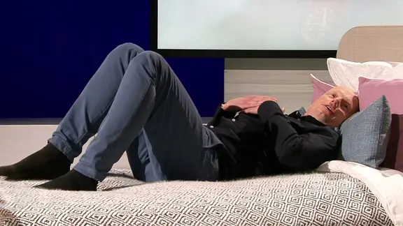 Dr. Helge Riepenhof, Orthopäde, Reha- und Sportmediziner im BG Klinikum Hamburg, liegt mit angewinkelten Beinen und verschränkten Händen auf dem Bauch auf einem Bett, umgeben von mehreren Kissen.