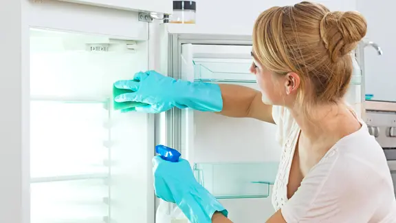 Eine Frau reinigt einen leeren Kühlschrank.