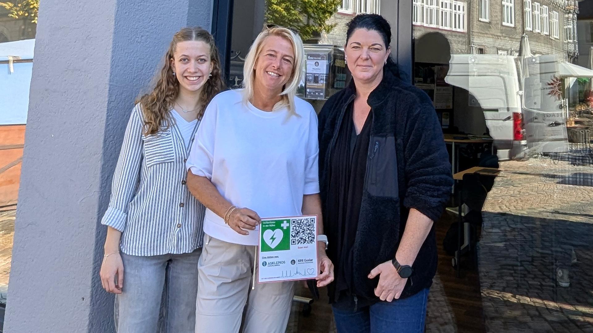Drei Frauen zeigen einen Aufkleber mit einem Defibrillator-Symbol. | Stadt Goslar