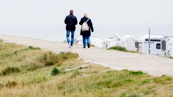 Touristen gehen bei trübem Wetter in Harlesiel auf einem Deich vor der Nordsee entlang. Niedersachsens Urlaubsregionen stellen sich auf viele Herbstferien-Urlauber ein.